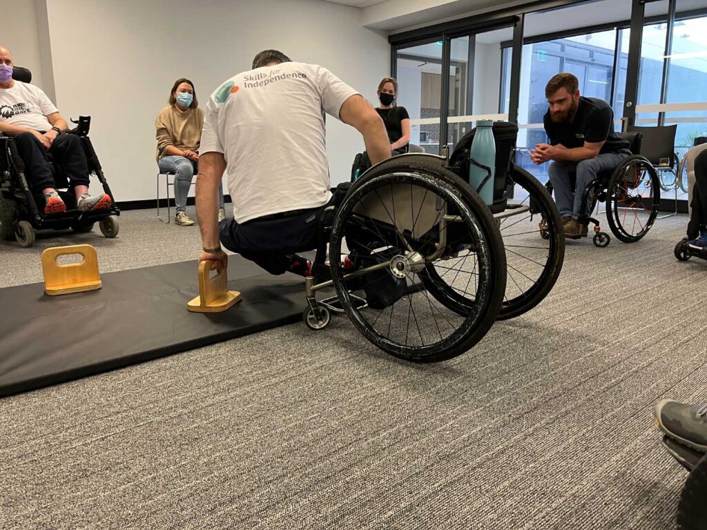 Peer-led program leaders demonstrating how to safely transfer from a wheelchair to the floor. Photo supplied by AQA Victoria.